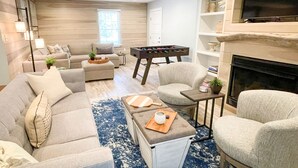 A modern living room with a sofa set, a coffee table, a foosball table, and a fireplace.