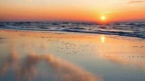 A beach with a sunset, calm water, and a clear sky.