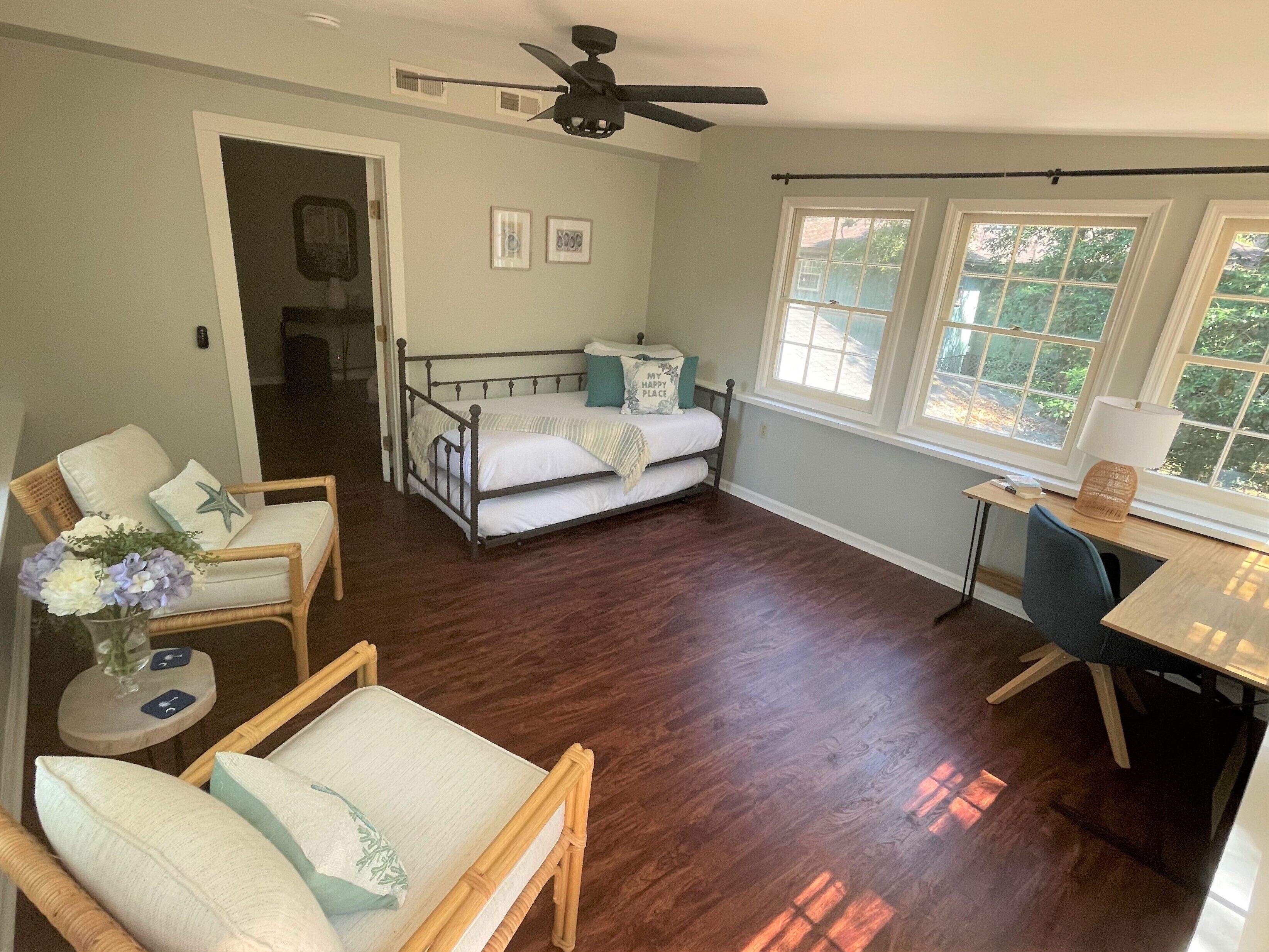 A spacious room with a bed, two chairs, a desk, and a ceiling fan.