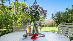 Une table à l’extérieur, avec un livre, un verre de vin, une bouteille et un vase de fleurs.