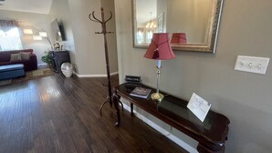 A living room with a dark wood floor, a red sofa, a coffee table, a lamp, a coat rack, and a mirror on the wall.