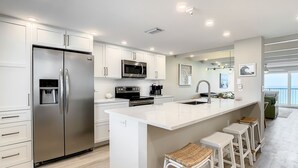 A modern kitchen with stainless steel appliances, white cabinetry, and a large island with bar stools.