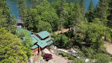 A lodge with a green roof, surrounded by dense forest and a lake.
