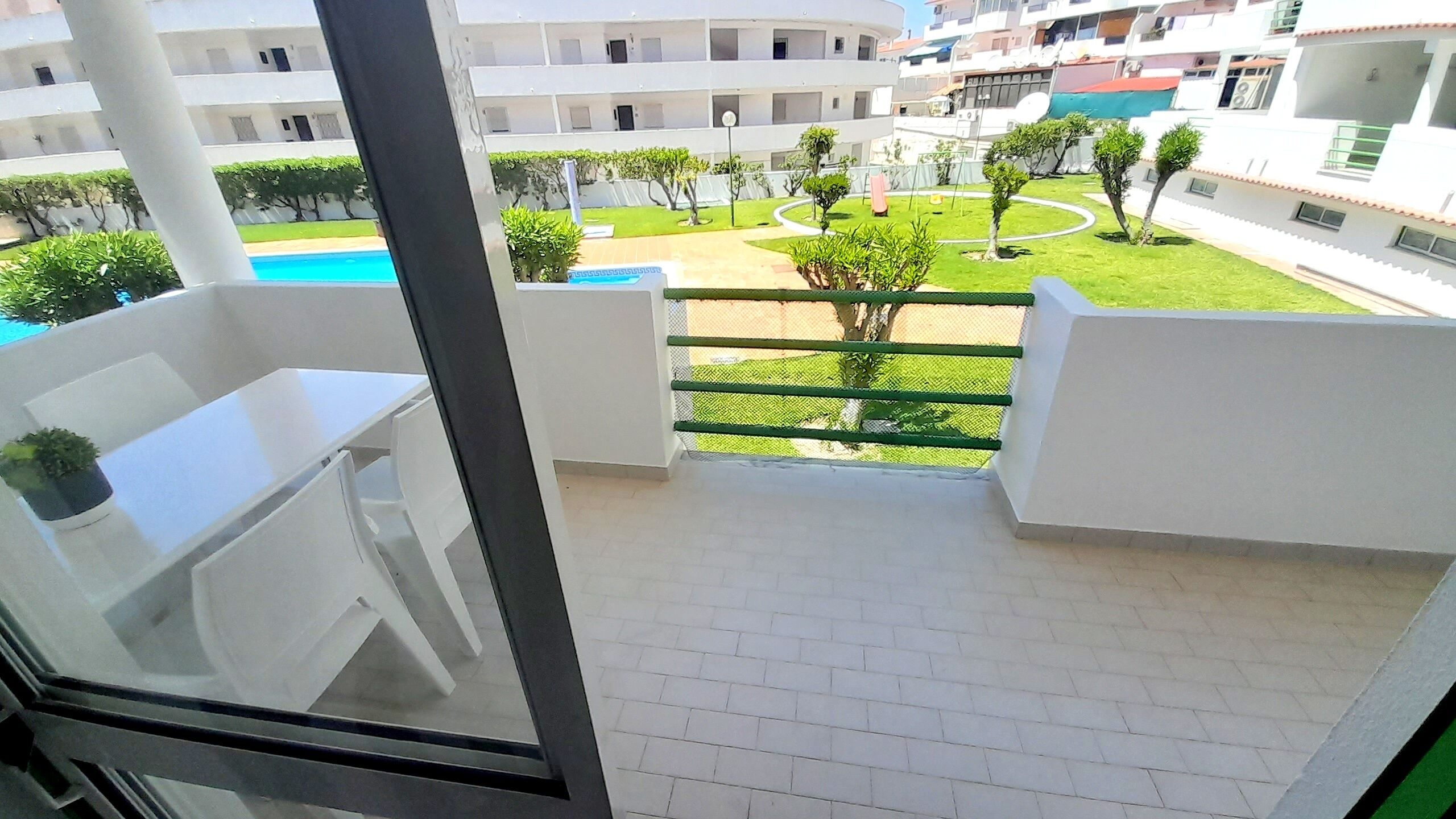 A balcony with a view of a swimming pool, a green lawn, and a white building in the background.