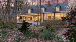 A two-story house with a porch, surrounded by trees and a garden. - Waterfront Paradise with Pool & Hot Tub plus 4 King Beds & 4 Full baths (Lexington Park)