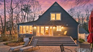 A modern house with a sloped roof, large windows, and a well-lit entrance. - Waterfront Paradise with Pool & Hot Tub plus 4 King Beds & 4 Full baths (Lexington Park)