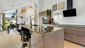 Une cuisine moderne dotée d’un îlot central, de tabourets de bar, de luminaires suspendus et d’une grande fenêtre donnant sur un jardin.