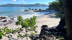 A beach with clear blue water, rocky shore, and lush greenery.