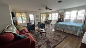 Una habitación amplia con una cama grande, un sofá rojo, dos sillones, una mesita y un ventilador de techo.