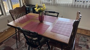Un comedor con una mesa de madera, individuales rojos y sillas. Un jarrón con flores amarillas está sobre la mesa.