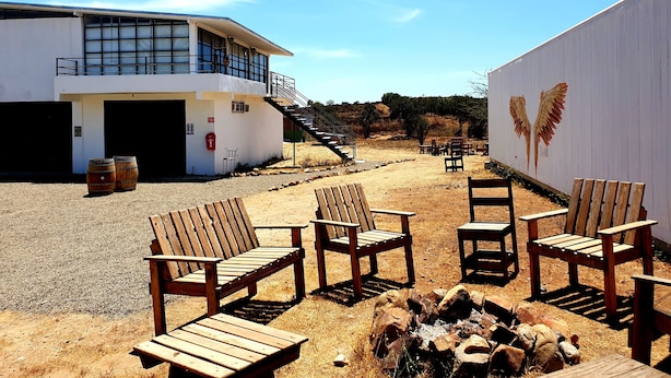 A building with a white exterior, a staircase leading to a balcony, and outdoor seating with wooden chairs and tables. - Wine country In Valle de Guadalupe (Valle de Guadalupe)