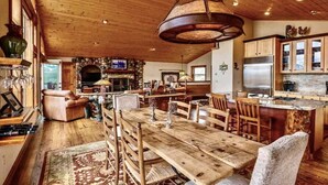 A rustic interior with a wooden dining table, chairs, a stone fireplace, and a kitchen area with modern appliances. - Hot Tub with Amazing Views- 7min to town/resort (Crested Butte)