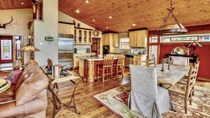 A spacious living room with a large sofa, a dining table with chairs, and a kitchen area with wooden cabinets and a central island. - Hot Tub with Amazing Views- 7min to town/resort (Crested Butte)