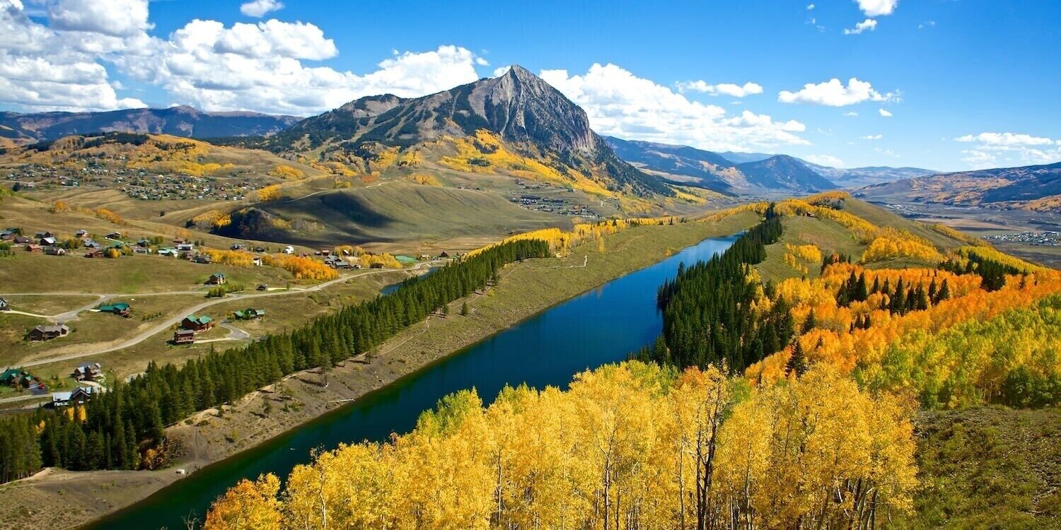 A mountainous landscape with a river, autumn foliage, and a small settlement with houses and roads.
