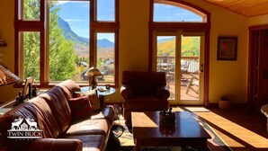 A cozy lodge room with a large window offering a scenic view of mountains and autumn foliage. - Hot Tub with Amazing Views- 7min to town/resort (Crested Butte)