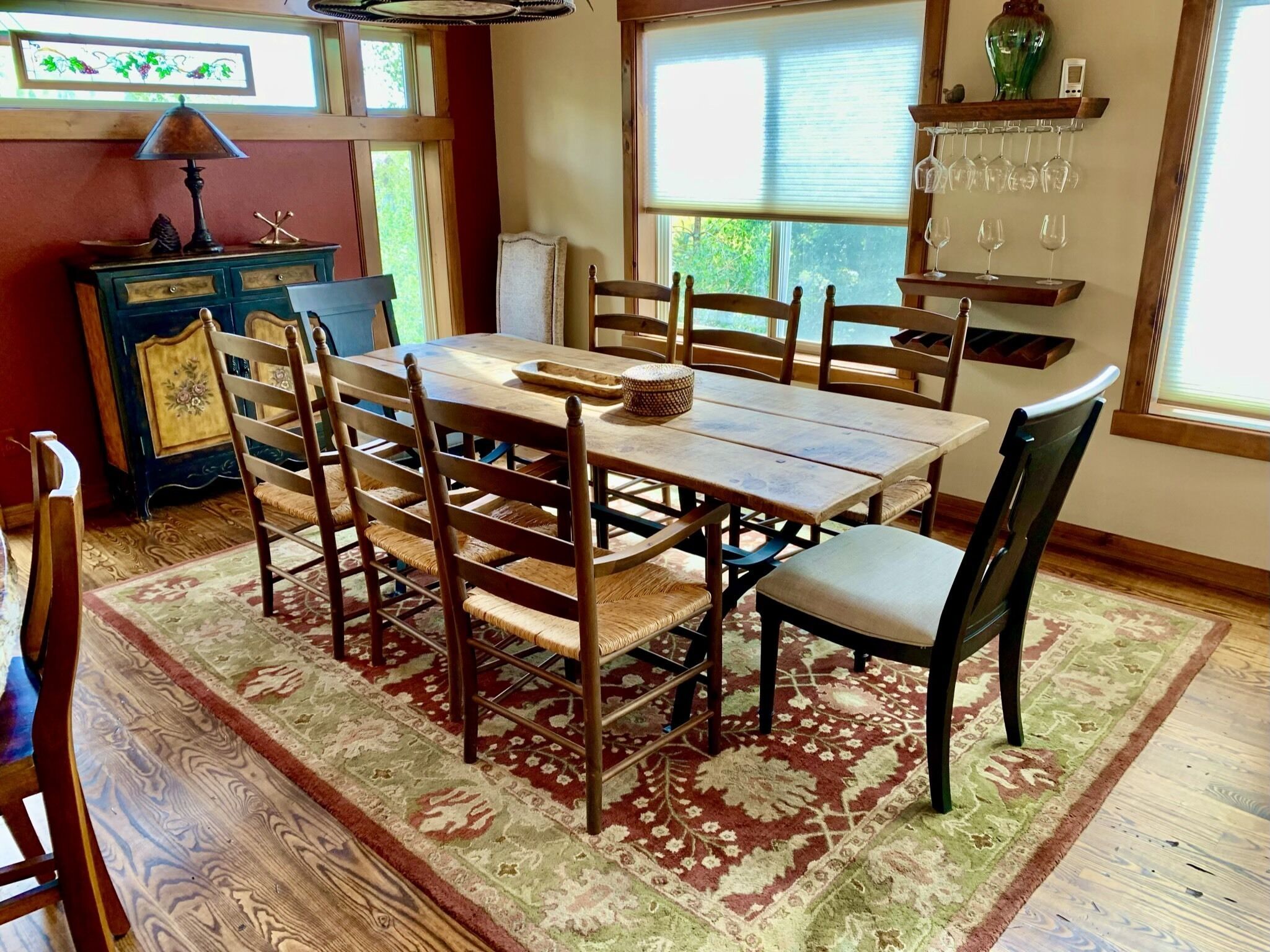 A dining area with a wooden table and chairs, a patterned rug, and a window with blinds.