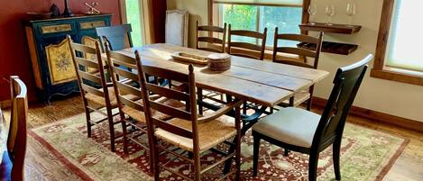 A dining area with a wooden table and chairs, a patterned rug, and a window with blinds.