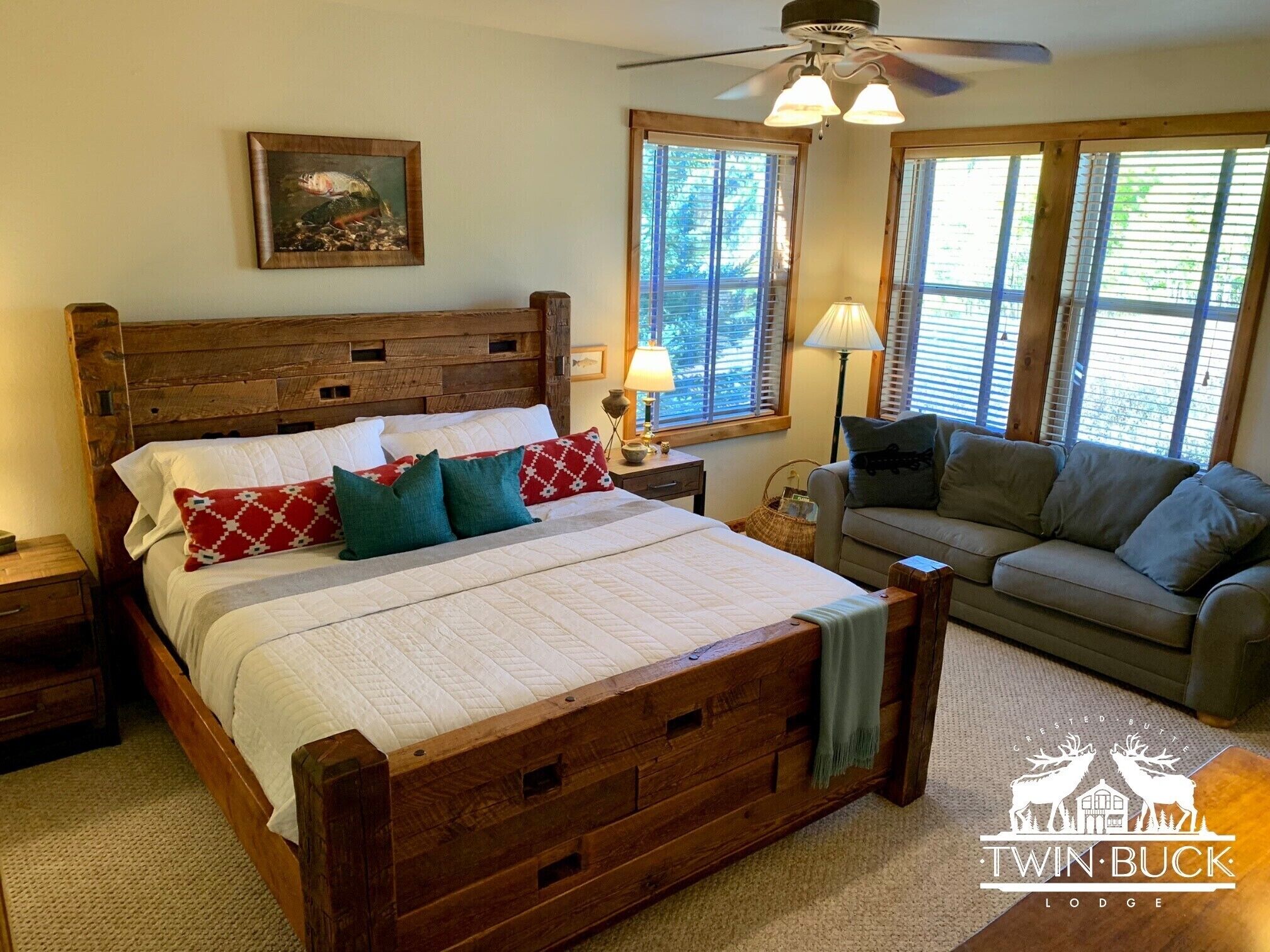 A bedroom with a wooden bed, a wooden headboard, a nightstand, a lamp, a window with blinds, and a couch.