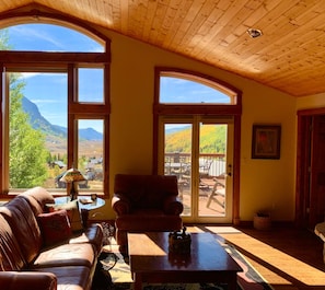 Une chambre confortable dans un chalet, dotée d’une grande fenêtre offrant une vue imprenable sur les montagnes et les couleurs automnales.