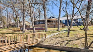 Un pont en bois enjambant un petit ruisseau, menant à un bâtiment doté d’une terrasse et d’un espace abrité.