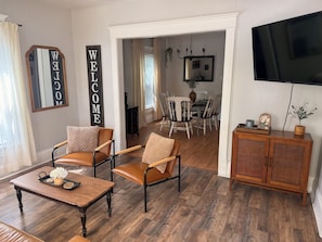 Una sala de estar con sillones de cuero, una mesa de centro de madera, un televisor y un comedor con una araña.