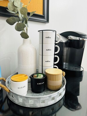 A coffee maker, a white mug, a black mug, a cream container, and a sugar container on a tray.