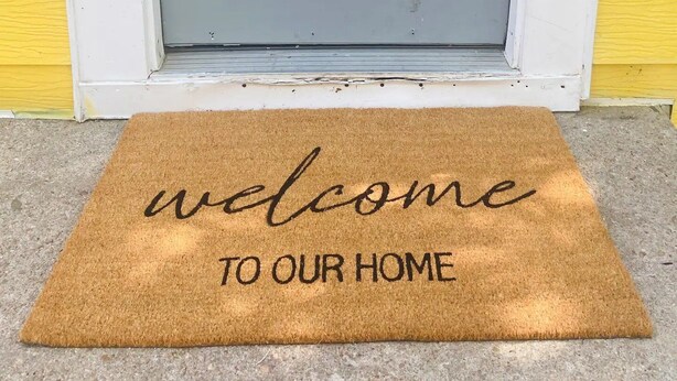 Una puerta gris con cerradura electrónica y un felpudo que dice 'welcome to our home'.