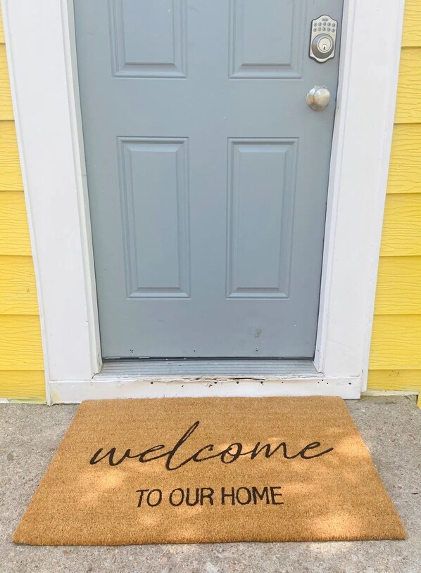 A grey door with a keypad lock and a doormat that reads "welcome to our home".