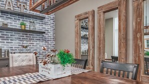 A dining area with a wooden table, white upholstered chairs, and a farmhouse-style decor including a brick wall and wooden beams. - 1000MBPS Wifi★One Story Luxury 5 Bedrooms Model Home (Jurupa Valley)