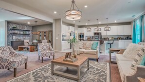 A spacious living room with a coffee table, sofas, and a kitchen in the background. - 1000MBPS Wifi★One Story Luxury 5 Bedrooms Model Home (Jurupa Valley)