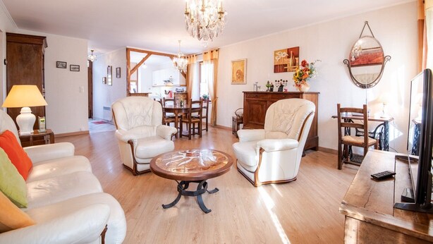 Un vaste salon agrémenté d’un lustre, de fauteuils en cuir, d’une table basse en bois et d’un coin repas avec un buffet et des chaises en bois.