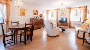 Un salon spacieux avec une table à manger en bois, deux canapés, un téléviseur et un lustre.