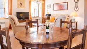 Un coin repas comprenant une table ronde en bois, six chaises, un lustre, un téléviseur et un canapé.