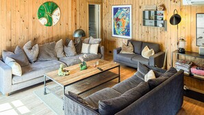 A living room with two sofas, a coffee table, and a wooden wall with a clock and artwork. - 5 bedroom nice home in Nexø (Nexø)