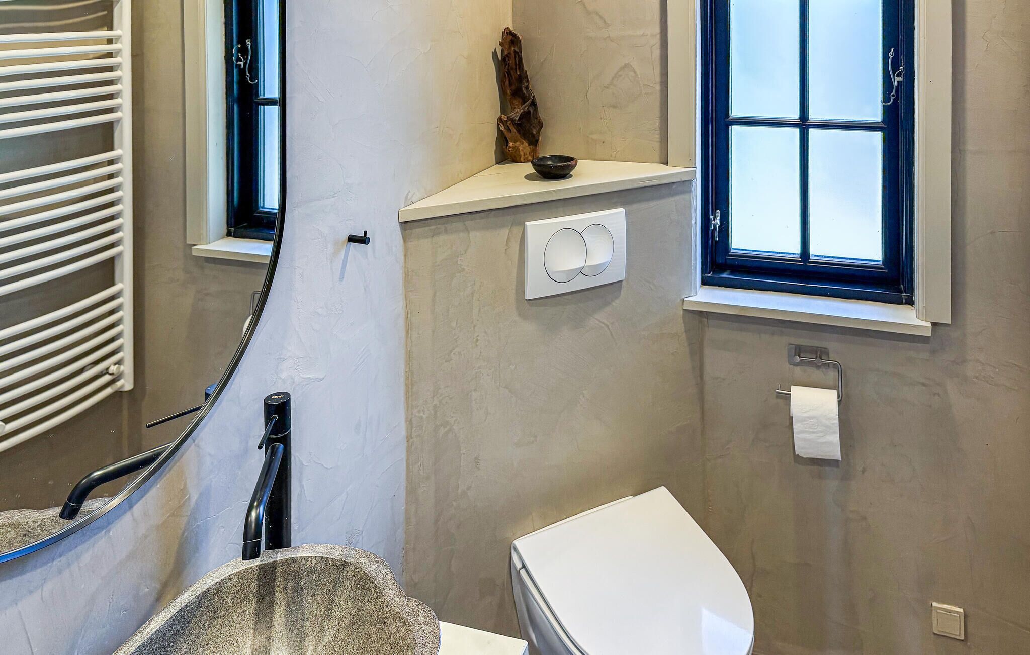 A bathroom with a toilet, a towel rack, a window, and a wall-mounted heater.