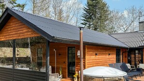 A wooden cabin with a sloped roof, large windows, and a patio area with outdoor furniture. - 5 bedroom nice home in Nexø (Nexø)