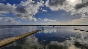 Una masa de agua tranquila con un muelle de madera que se adentra en ella, rodeada por un cielo nublado.