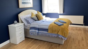 Un dormitorio con cama, mesita de noche, cómoda, ventana con cortinas y un radiador.