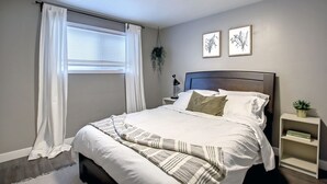 Un letto rifatto con biancheria bianca e una coperta decorata, un comodino con una lampada e una piccola pianta.