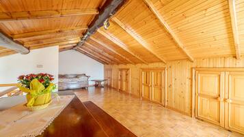 Ein geräumiges Dachzimmer mit Holzwänden und -decke, einem langen Holztisch und einem Sofa.