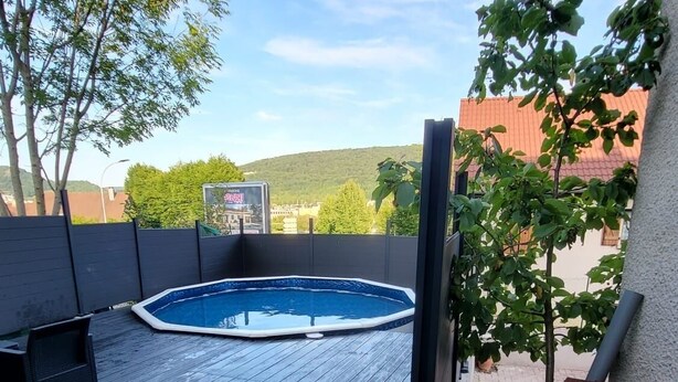 A backyard with a hot tub, wooden deck, and a view of a hill. - Pro home (Besançon)
