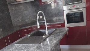 A kitchen with a granite countertop island, stainless steel appliances, and red cabinetry. - Pro home (Besançon)