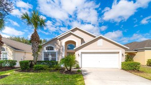 A single-story house with a garage, a small front yard with a palm tree, and a clear blue sky.