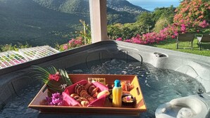Ein Whirlpool mit einer Serviertablett voller Snacks und Blumen, umgeben von üppiger Vegetation und einer schönen Aussicht.