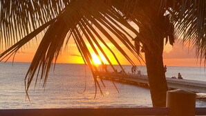Sonnenuntergangsblick vom Strand mit Palmen und einem Steg.