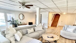 Un salon spacieux avec un canapé d’angle gris, une table basse ronde et un ventilateur de plafond.