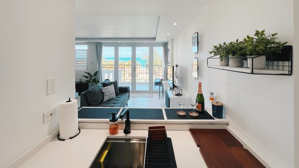 Eine moderne Küche mit Spüle, Armatur und Arbeitsplatte. Es gibt einen Essbereich mit Tisch und Stühlen, sowie einen Balkon mit Meerblick.