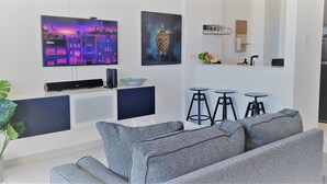 Ein modernes Wohnzimmer mit einem grauen Sofa, einem Flachbildfernseher und einem wandmontierten Regal mit Dekorationselementen.