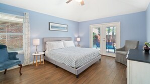 Een slaapkamer met een bed, een plafondventilator, een raam met jaloezieën, een stoel en uitzicht op de omgeving.