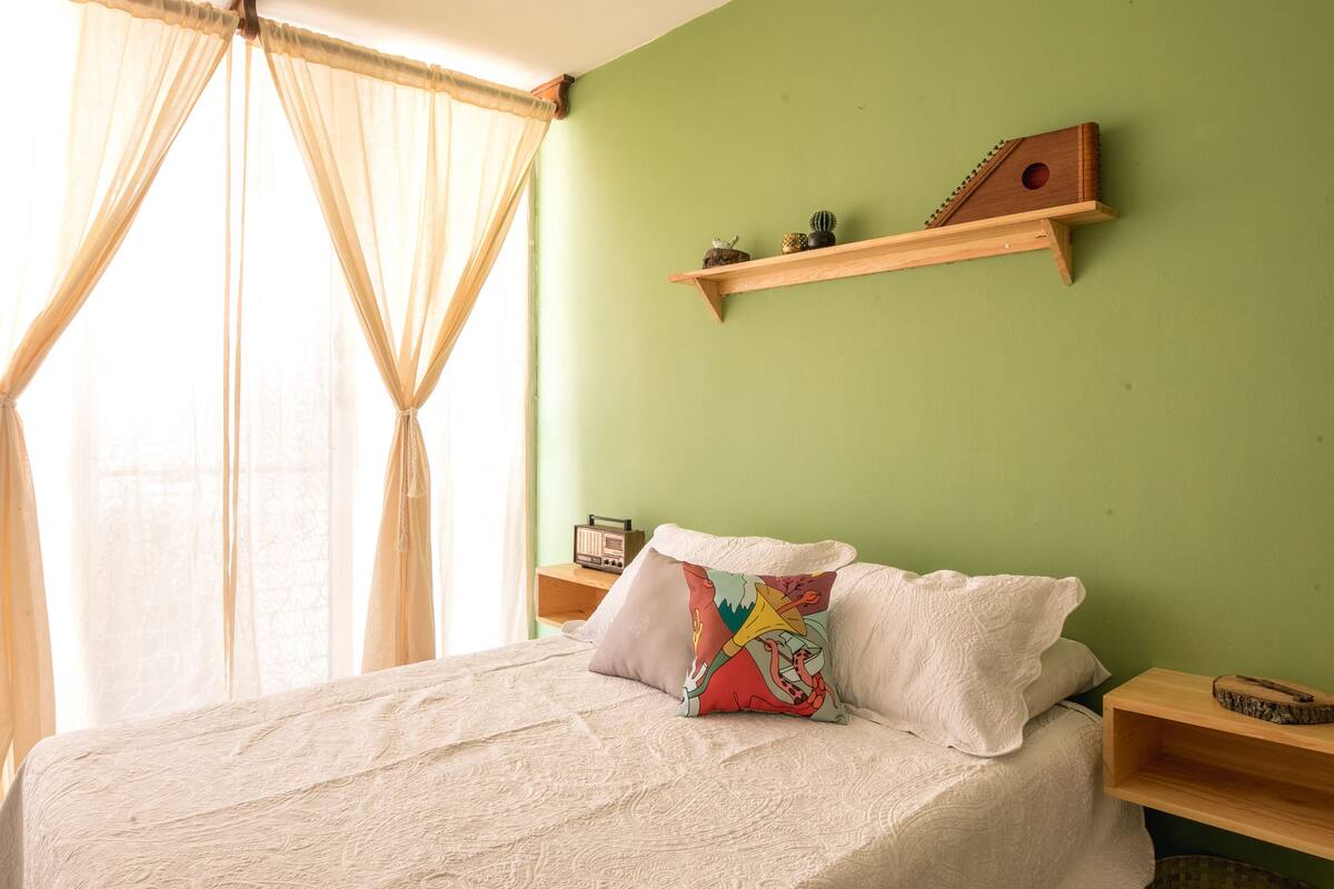 A bedroom with a bed, a bedside table, a radio, and a shelf with decorative items.